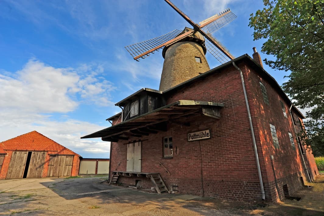 Historische Pottmühle aus rotem Backstein mit hölzernen Flügeln und angrenzendem Schuppen.
